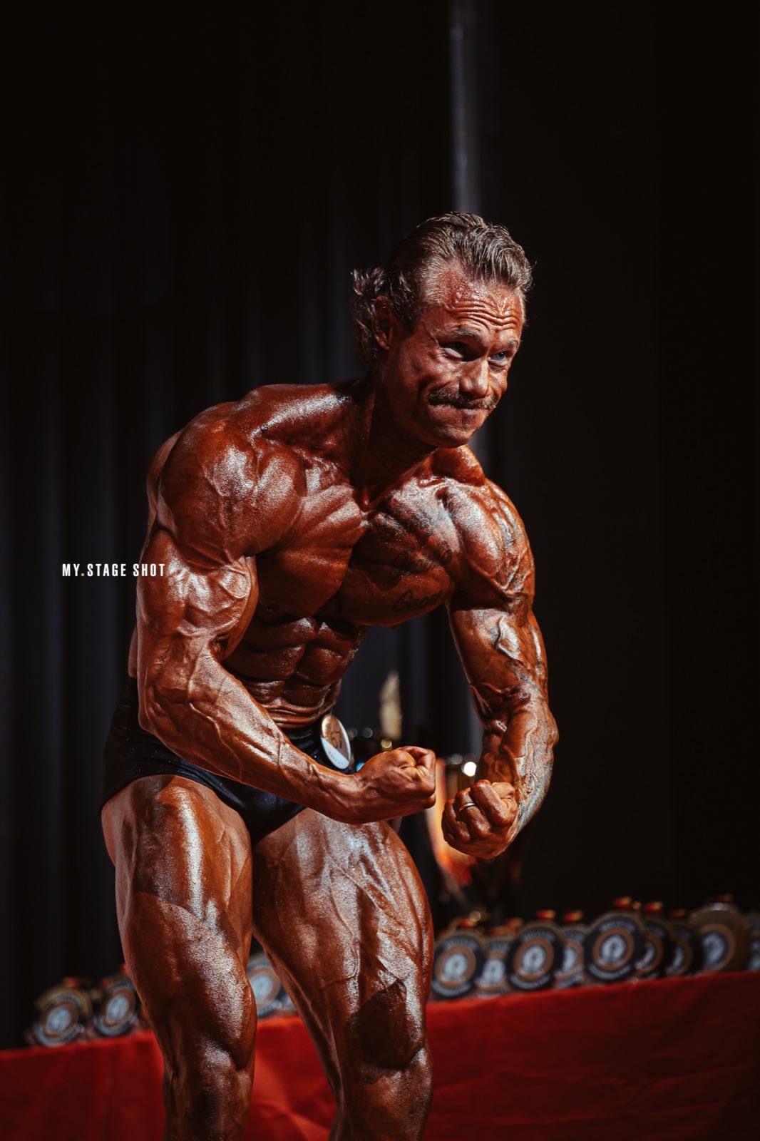 Bodybuilder posiert vor dem Tisch mit den Pokalen