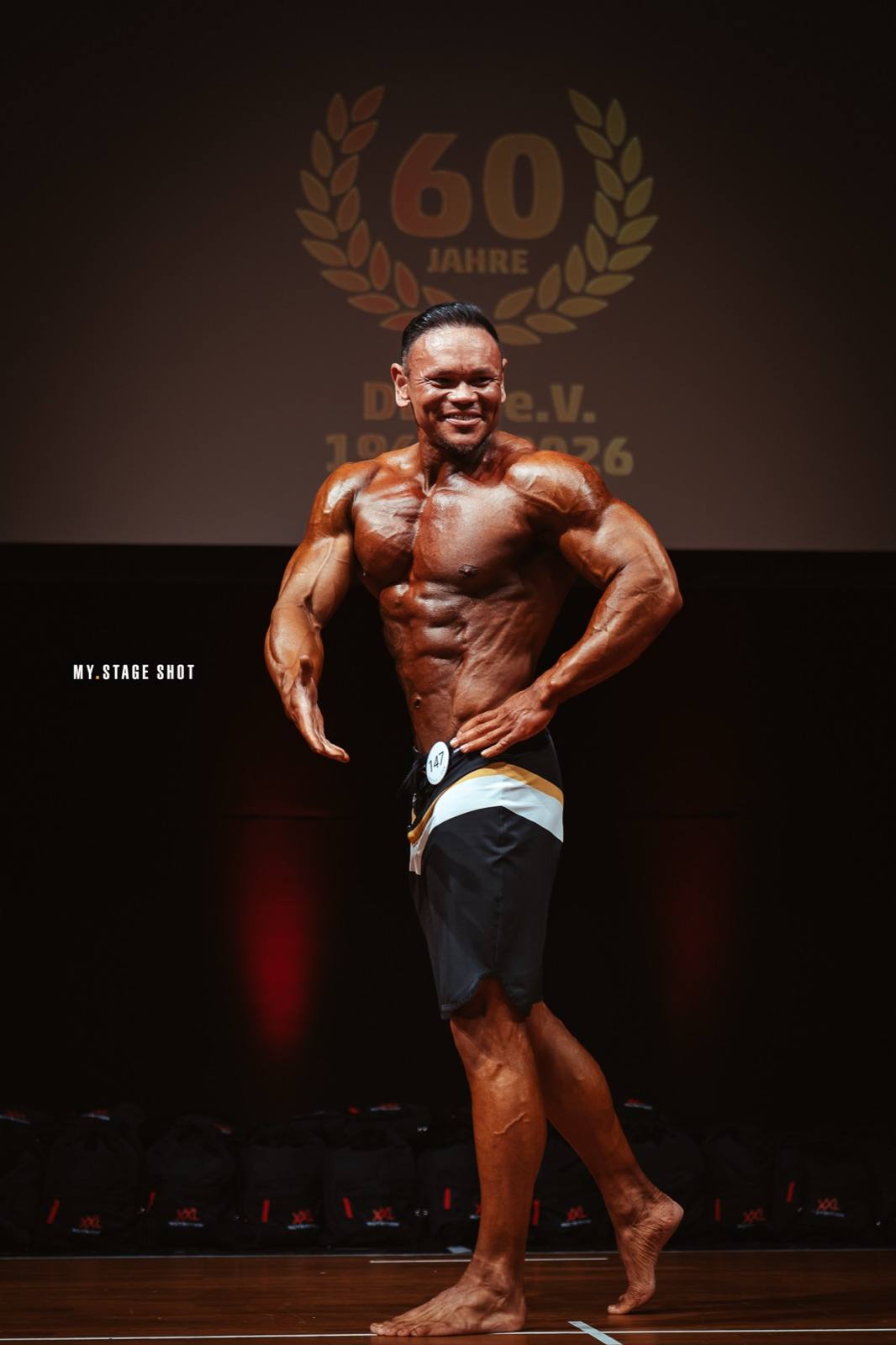 Bodybuilder in der Frontpose vor der Jubiläumswand zum 60-jährigen Bestehen