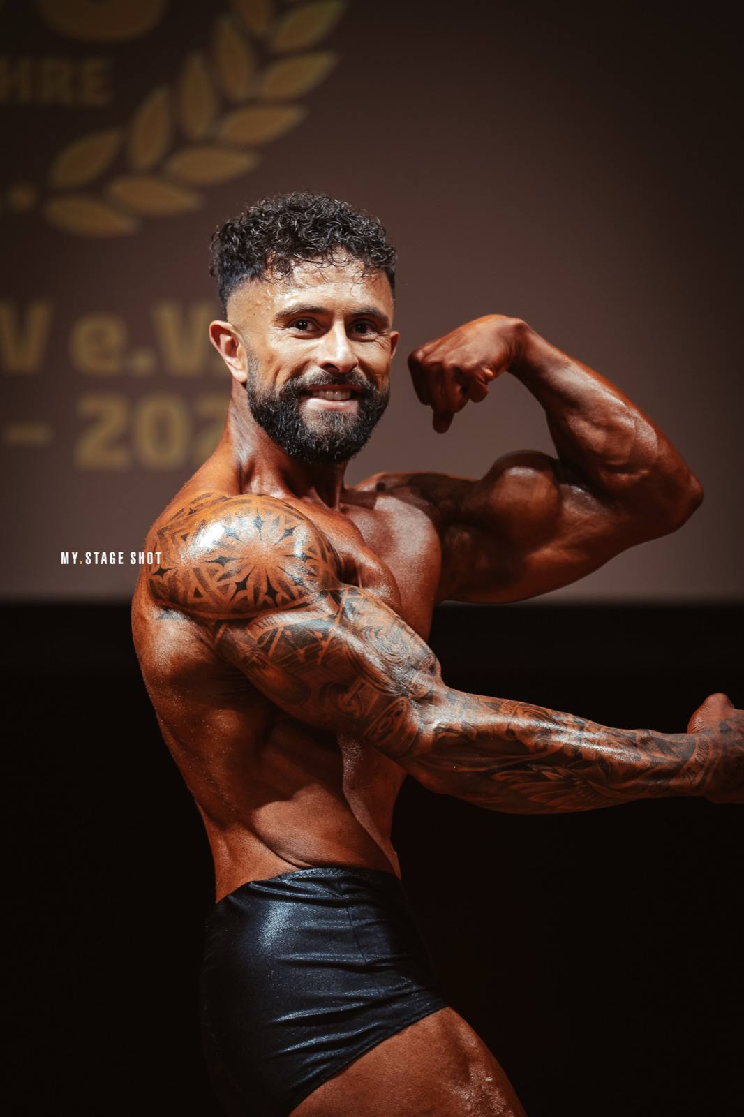 Tätowierter Bodybuilder in der Bizeps-Pose vor der Jubiläumswand